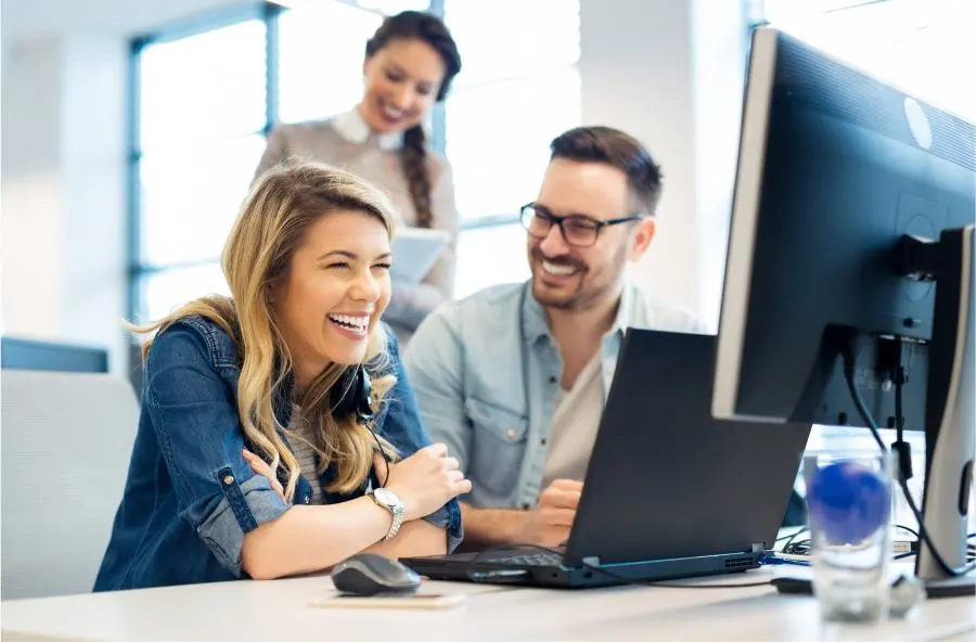 Una donna e un uomo siedono ridendo davanti a un computer.